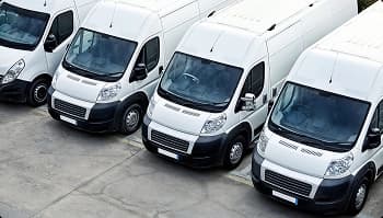 Row of white cargo vans parked in an industrial lot for fleet service