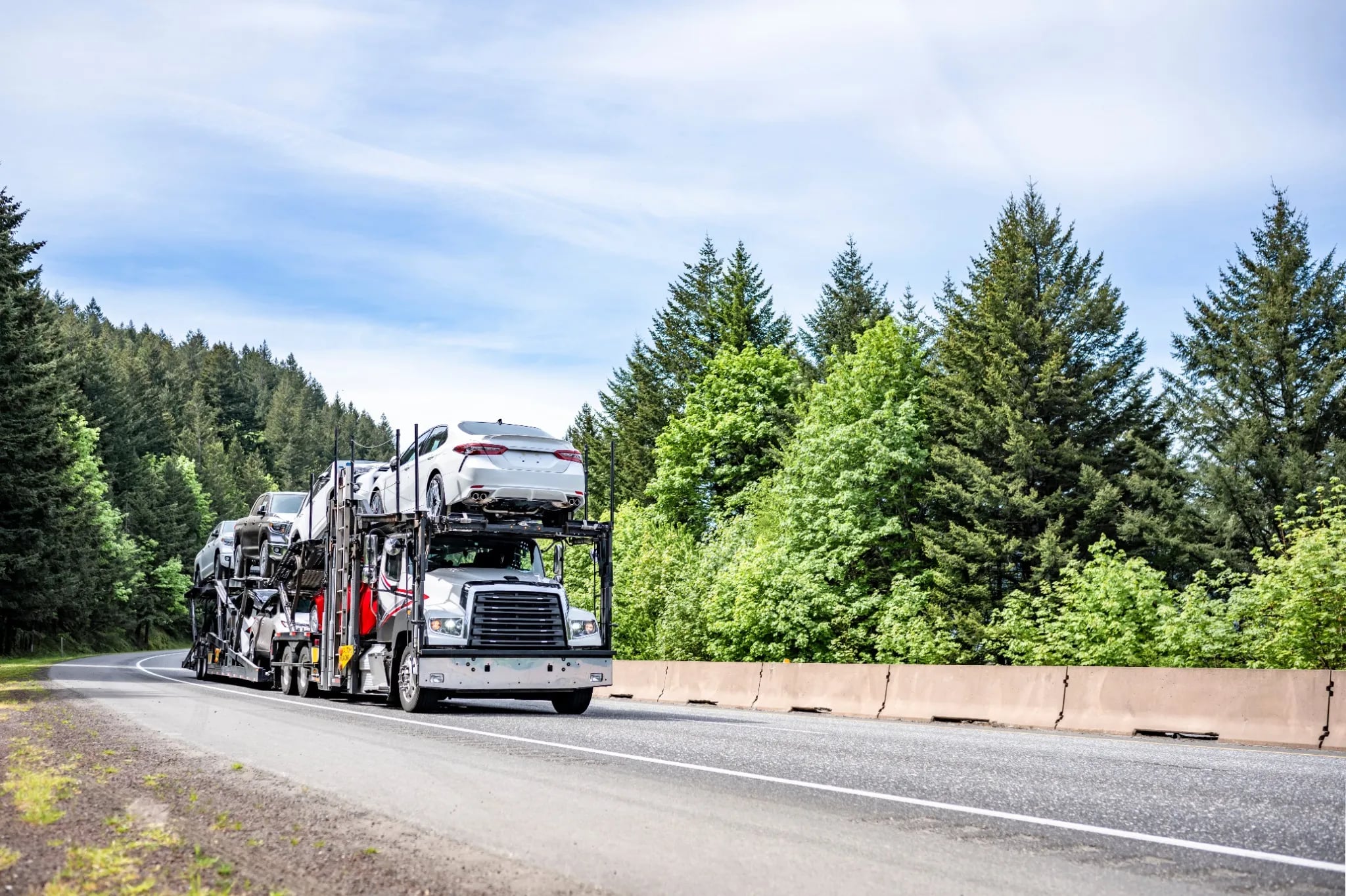 open car carrier transporting sedans on a highway for nationwide door to door auto transport