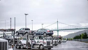 Auto transport staging yard Multiple open car carriers parked near a suspension bridge on an overcast day