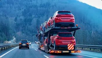 Open carrier auto transport Loaded open car carrier hauling red SUVs on a mountain highway at dusk