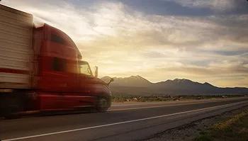 Nationwide auto transport Red semi truck driving on a highway with mountains and sunset in background