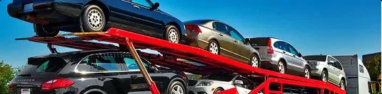 Open carrier car shipping on red multi car hauler row of sedans on red open car carrier under clear blue sky for affordable car shipping
