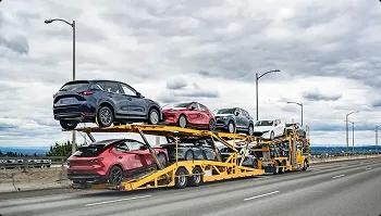 Yellow open carrier transporting vehicles yellow open car hauler transporting SUVs and sedans on a highway