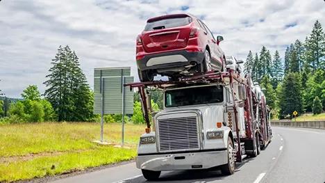 Open Carrier Auto Transport White semi car hauler carrying a red SUV on an open trailer along a highway with trees