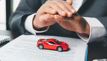 Insured transport protection for luxury vehicles hands covering small red sports car over paperwork symbolizing insured transport protection