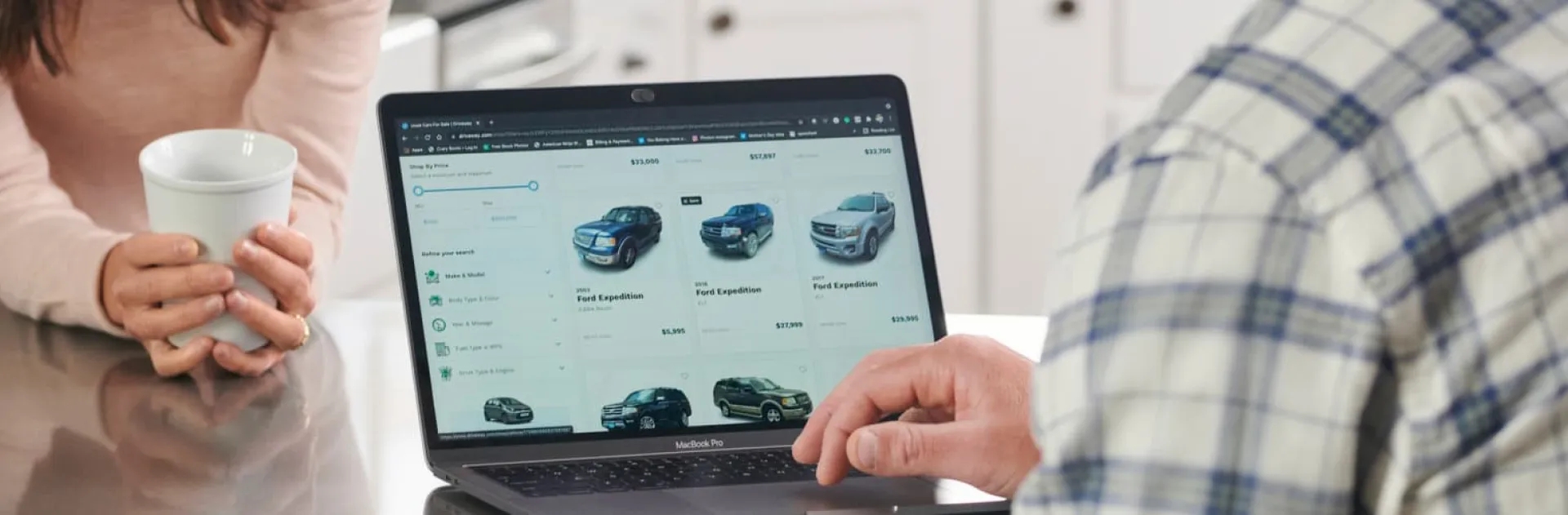 Online car buyers and sellers transport service person viewing online car listings on laptop with coffee cup nearby