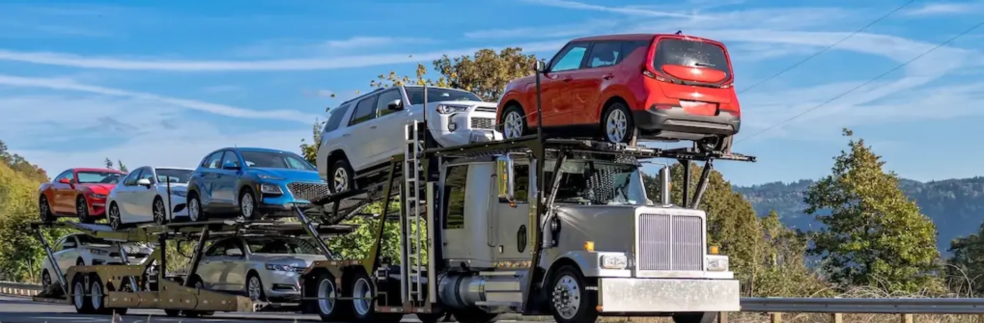 Open auto transport hero open car carrier loaded with multiple vehicles under clear sky background