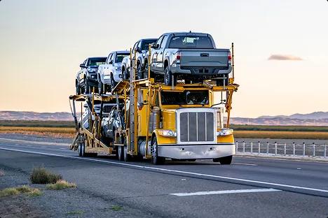 Open carrier car shipping on highway at sunset yellow open car carrier hauling pickup trucks on highway at sunset showing door to door auto transport