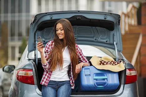 Student loading car for move college student sitting on car trunk with luggage checking phone before move