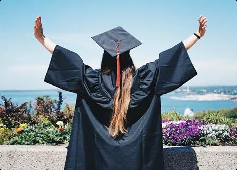 Student graduation celebration student in graduation cap raising arms overlooking campus and water