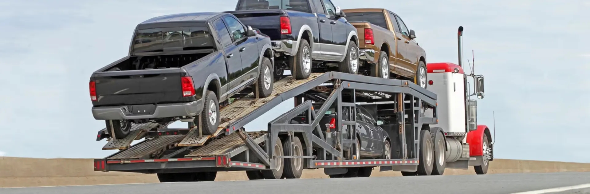 Truck shipping services for pickups and work trucks open car carrier hauling pickup trucks on highway representing truck shipping services