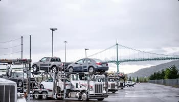 Auto transport staging yard Multiple open car carriers parked near a suspension bridge on an overcast day