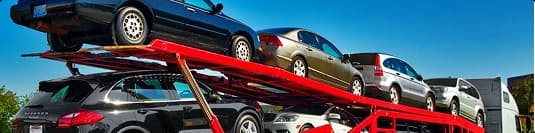 Open carrier loading for reseller auto transport row of cars on red open carrier at dealership lot for reseller auto transport