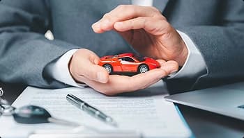 Full insurance coverage and protection hands protecting small red sports car over paperwork symbolizing insured transport