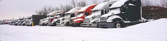 Winter conditions affecting car shipping row of semitrucks parked in snow showing winter car shipping conditions