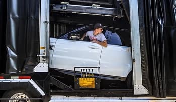 Enclosed car loading driver inside driver carefully loading white car into enclosed auto transport trailer