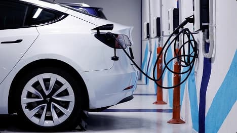 Electric Vehicle Shipping White Tesla sedan charging at an indoor EV station with cables connected