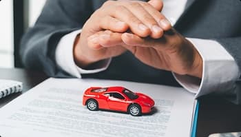 Insured transport protection for luxury vehicles hands covering small red sports car over paperwork symbolizing insured transport protection