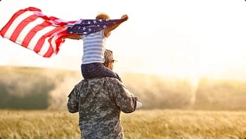 Family focused military car shipping service member carrying child with us flag in a field at sunset symbolizing pcs support