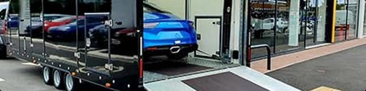 Enclosed car trailer loading vehicle enclosed car trailer loading blue vehicle at dealership entrance