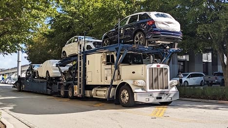 Open carrier delivery for dealership vehicles white semi car hauler transporting wrapped suvs on a city street for dealership delivery